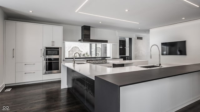 kitchen featuring sink, white cabinets, a large island, and wall chimney range hood