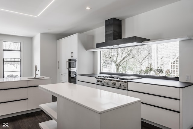 kitchen featuring a kitchen island, sink, stainless steel gas cooktop, white cabinets, and wall chimney exhaust hood