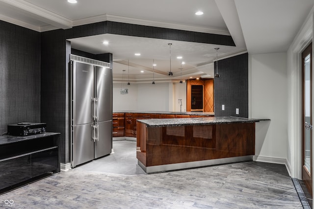 kitchen with decorative light fixtures, kitchen peninsula, sink, built in refrigerator, and dark stone counters