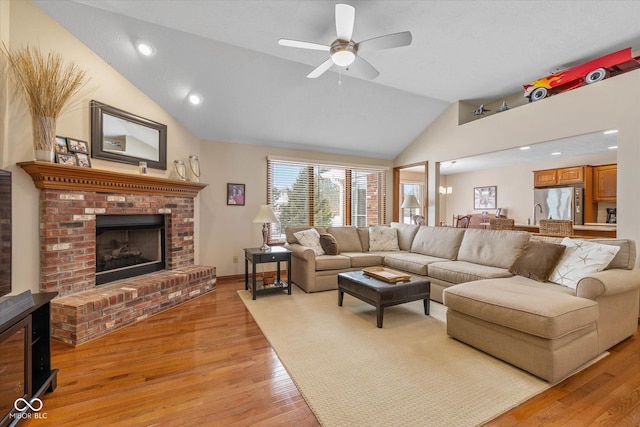 living room with lofted ceiling, light wood-type flooring, a brick fireplace, and ceiling fan