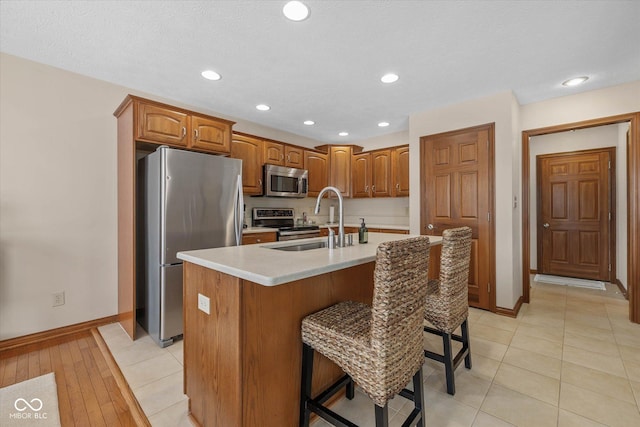 kitchen featuring sink, light tile patterned flooring, an island with sink, a breakfast bar area, and stainless steel appliances