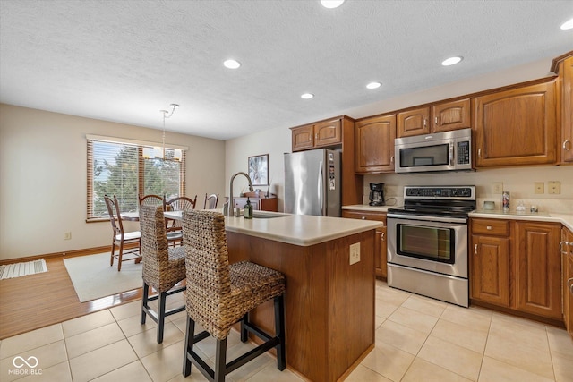 kitchen with light tile patterned floors, an island with sink, stainless steel appliances, decorative light fixtures, and sink