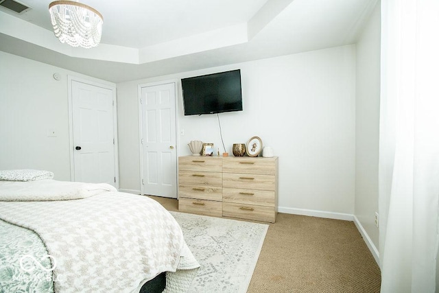 bedroom featuring a raised ceiling, a notable chandelier, and carpet flooring