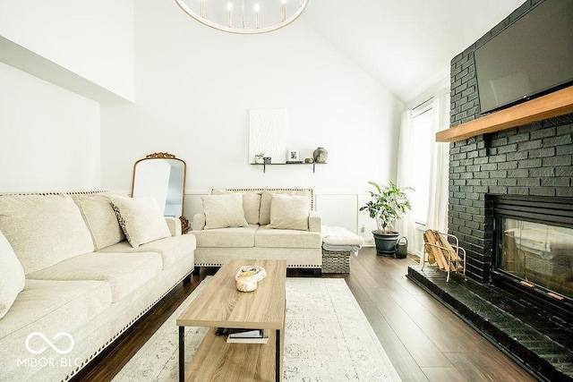 living room featuring high vaulted ceiling, a brick fireplace, a notable chandelier, and dark hardwood / wood-style floors