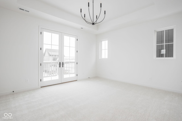 carpeted empty room featuring a raised ceiling, french doors, and a chandelier