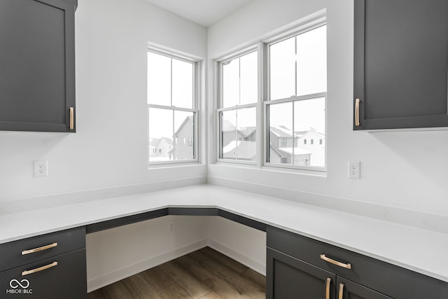 unfurnished office featuring built in desk and dark hardwood / wood-style floors