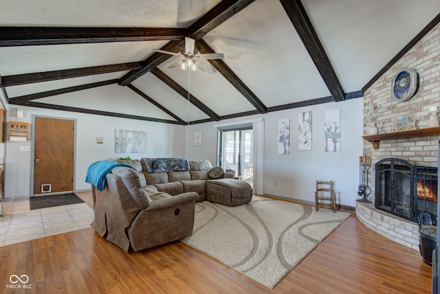 living room featuring light hardwood / wood-style flooring, ceiling fan, a fireplace, and vaulted ceiling with beams