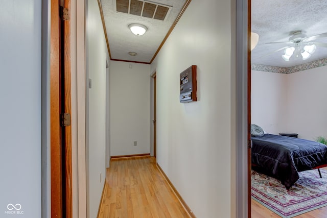 corridor featuring a textured ceiling, light hardwood / wood-style flooring, and ornamental molding