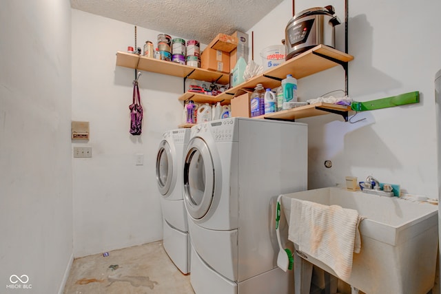 clothes washing area with washer and clothes dryer, sink, and a textured ceiling