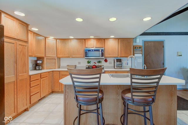 kitchen with a kitchen bar, sink, light brown cabinetry, and an island with sink