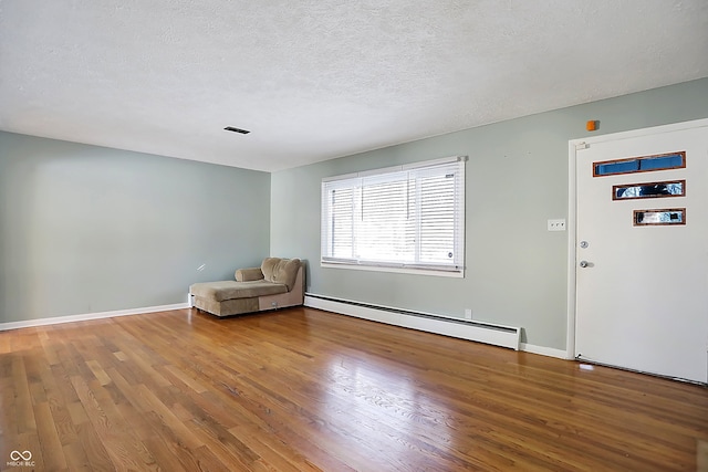 unfurnished room with a baseboard heating unit, hardwood / wood-style floors, and a textured ceiling