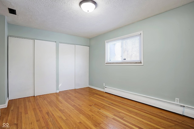 unfurnished bedroom with multiple closets, a textured ceiling, baseboard heating, and light hardwood / wood-style floors