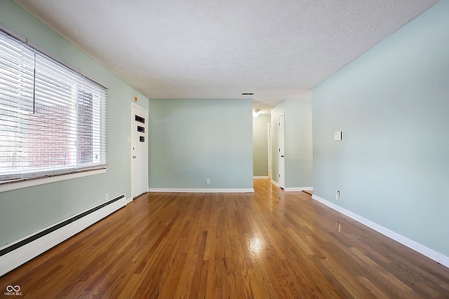 empty room with a textured ceiling, a baseboard radiator, and wood-type flooring