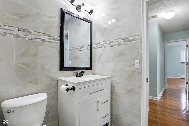 bathroom featuring toilet, a textured ceiling, tile walls, vanity, and hardwood / wood-style floors