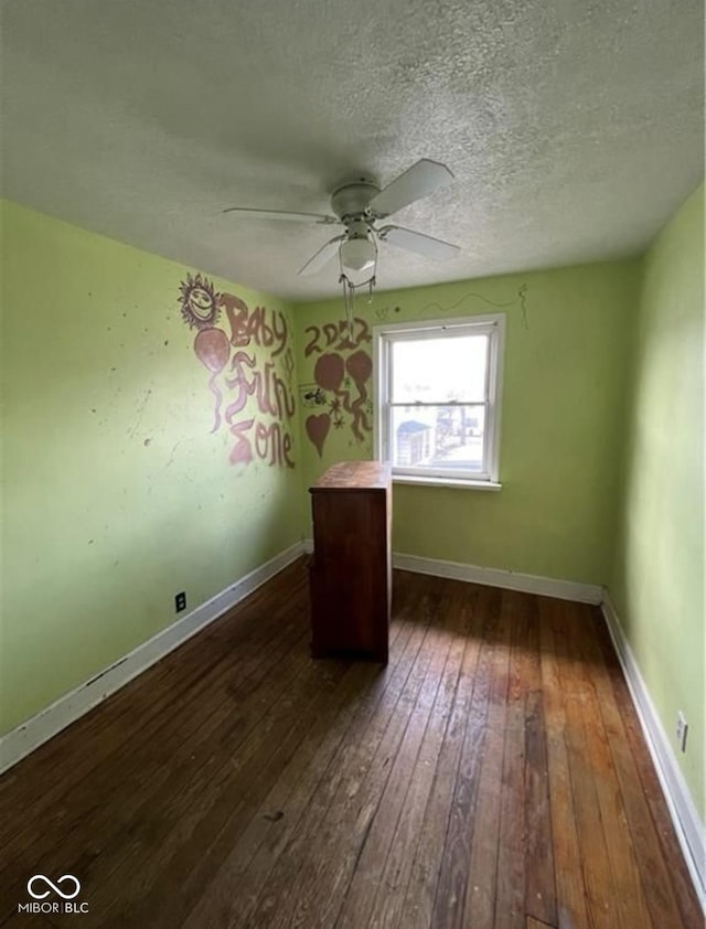 empty room featuring ceiling fan, dark wood-type flooring, and a textured ceiling