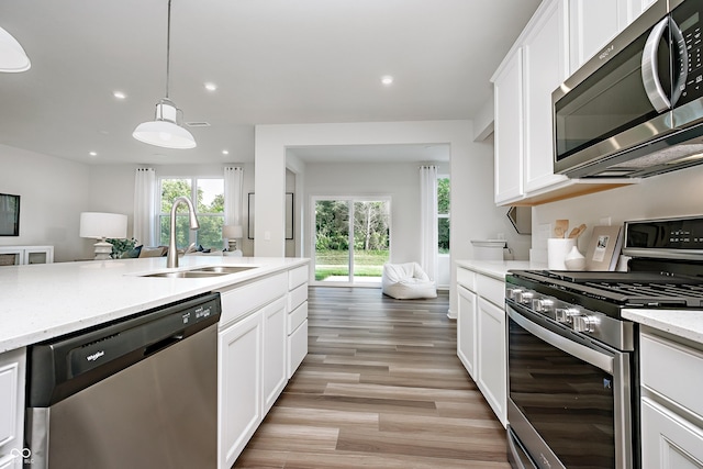 kitchen with light stone counters, decorative light fixtures, stainless steel appliances, white cabinets, and sink