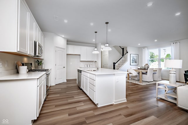 kitchen with an island with sink, appliances with stainless steel finishes, hanging light fixtures, and white cabinetry