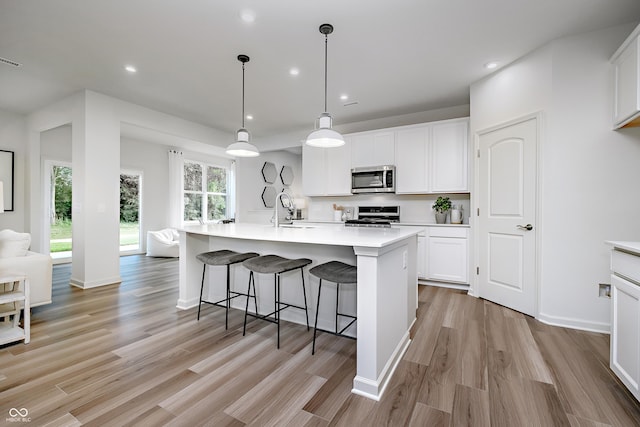 kitchen with a kitchen island with sink, stainless steel appliances, pendant lighting, sink, and white cabinetry