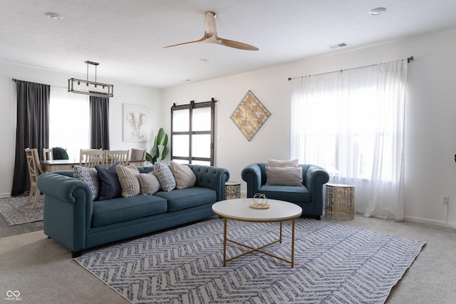 living room with ceiling fan, a barn door, visible vents, and a healthy amount of sunlight