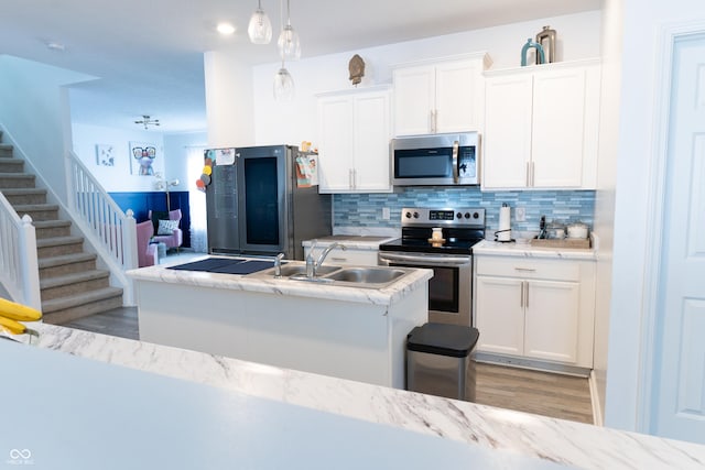 kitchen with sink, white cabinets, backsplash, hanging light fixtures, and stainless steel appliances