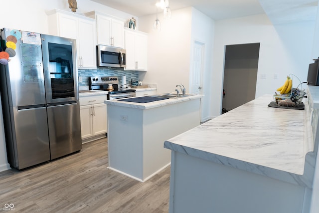 kitchen with light wood-type flooring, white cabinets, stainless steel appliances, a kitchen island with sink, and backsplash