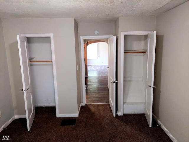 unfurnished bedroom with a textured ceiling, multiple closets, and dark colored carpet