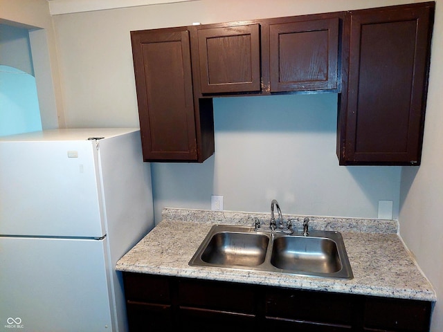 kitchen featuring sink, light stone countertops, white fridge, and dark brown cabinetry