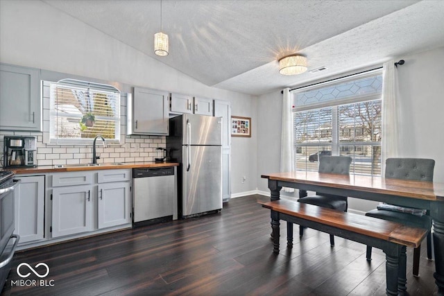 kitchen with lofted ceiling, dark hardwood / wood-style flooring, butcher block counters, stainless steel appliances, and hanging light fixtures