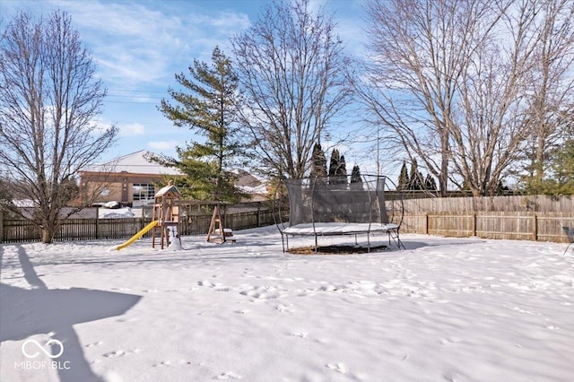 yard layered in snow featuring a playground and a trampoline