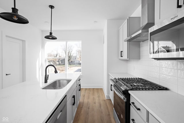 kitchen featuring wall chimney exhaust hood, pendant lighting, gray cabinets, appliances with stainless steel finishes, and sink