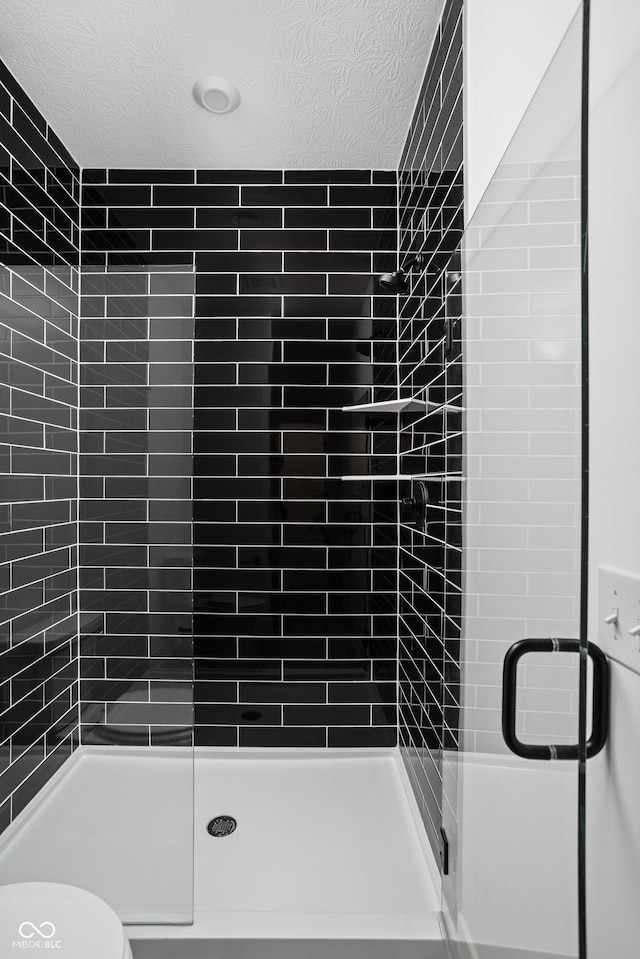 bathroom with a textured ceiling, a shower with door, and toilet