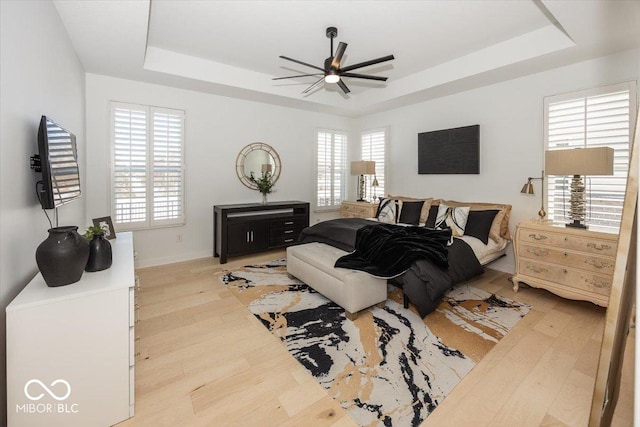 bedroom featuring ceiling fan, light hardwood / wood-style flooring, and a raised ceiling