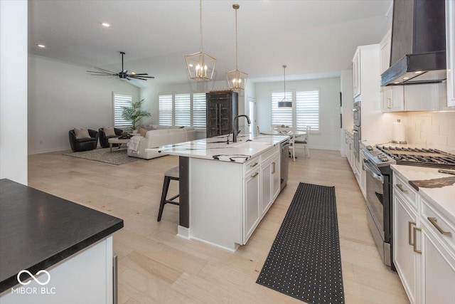 kitchen featuring a center island with sink, stainless steel appliances, hanging light fixtures, custom range hood, and white cabinets