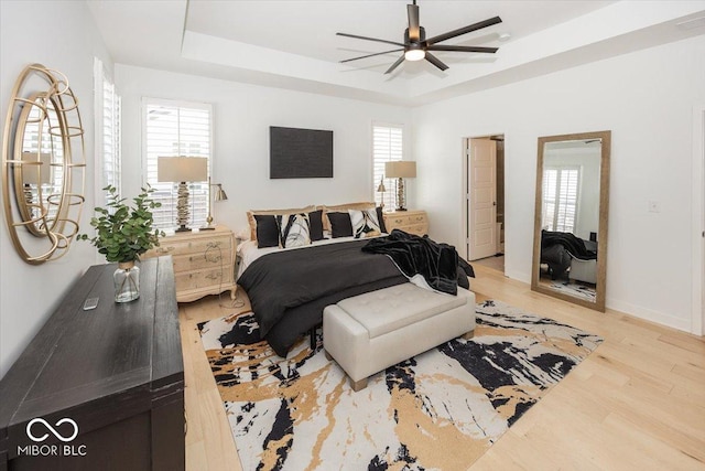 bedroom featuring ceiling fan, light wood-type flooring, and a tray ceiling