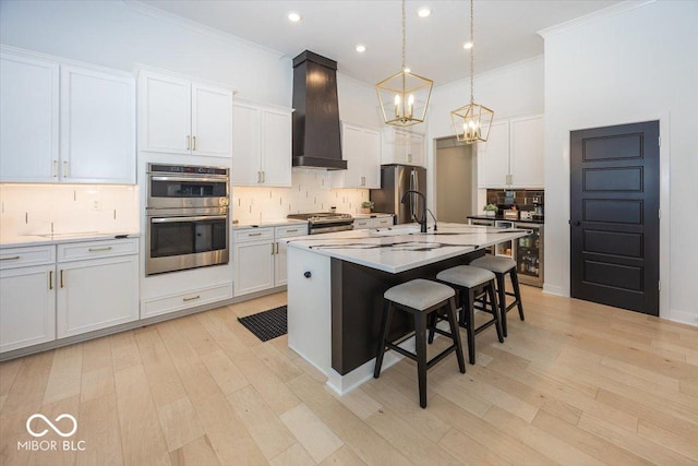 kitchen featuring white cabinetry, custom exhaust hood, an island with sink, stainless steel appliances, and pendant lighting