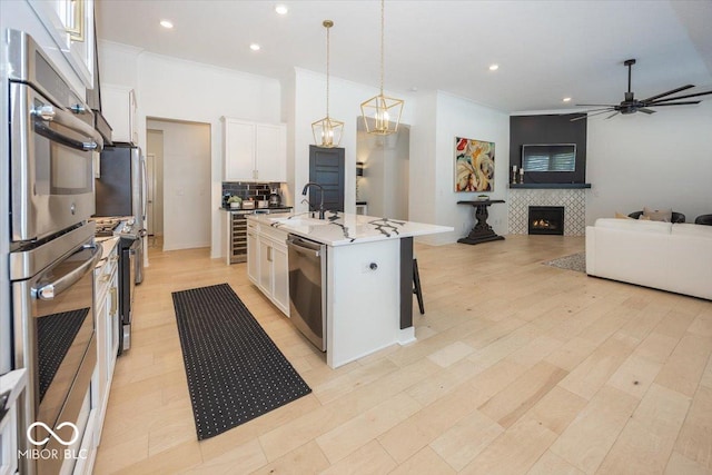 kitchen with a tile fireplace, hanging light fixtures, an island with sink, stainless steel appliances, and white cabinets