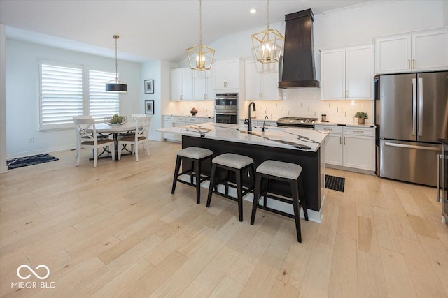 kitchen featuring a center island with sink, stainless steel appliances, custom range hood, white cabinets, and light stone counters