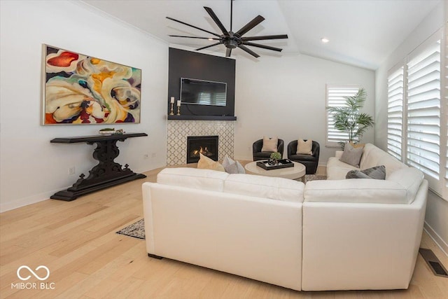 living room with light wood-type flooring, ceiling fan, vaulted ceiling, and a tile fireplace