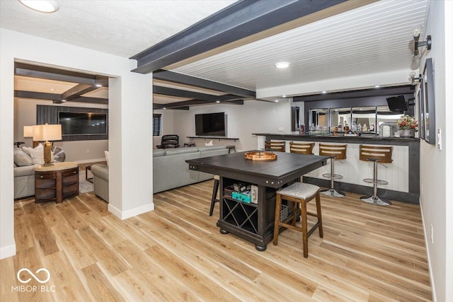 kitchen featuring light hardwood / wood-style floors, beam ceiling, kitchen peninsula, and a breakfast bar