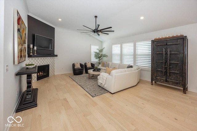 living room with ceiling fan, a tiled fireplace, vaulted ceiling, and light hardwood / wood-style flooring