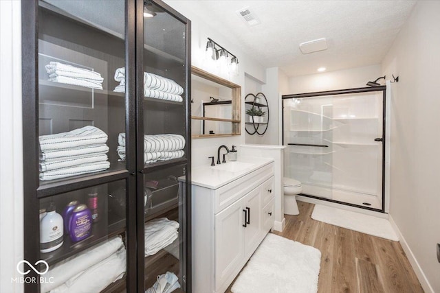 bathroom featuring toilet, wood-type flooring, walk in shower, a textured ceiling, and vanity