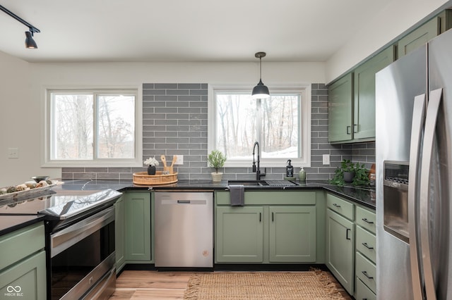 kitchen with hanging light fixtures, green cabinetry, backsplash, appliances with stainless steel finishes, and sink