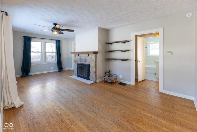 unfurnished living room with a textured ceiling, ceiling fan, light hardwood / wood-style floors, and a stone fireplace