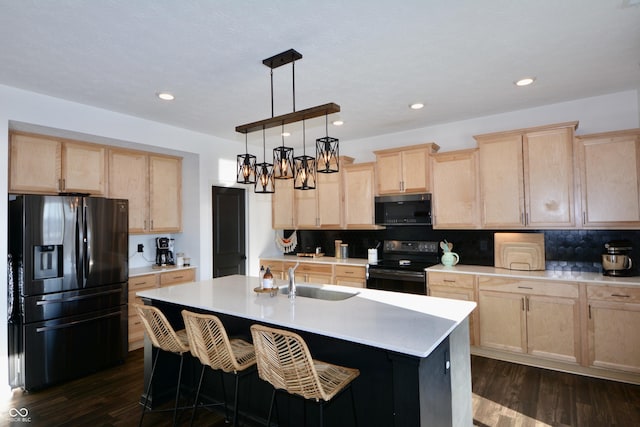 kitchen with sink, refrigerator with ice dispenser, an island with sink, hanging light fixtures, and black range with electric stovetop