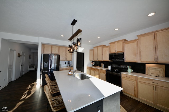 kitchen with sink, pendant lighting, black appliances, light brown cabinetry, and a kitchen island with sink