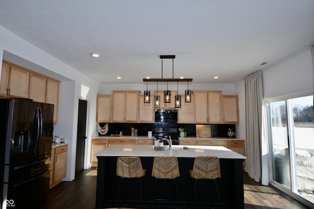 kitchen with electric range, an island with sink, black fridge, pendant lighting, and backsplash