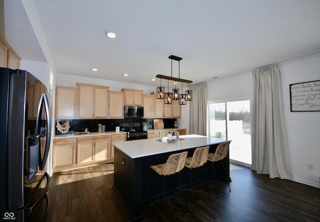 kitchen with black appliances, pendant lighting, light brown cabinetry, and a center island with sink