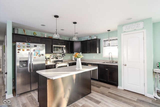 kitchen featuring appliances with stainless steel finishes, a center island, sink, hanging light fixtures, and light wood-type flooring