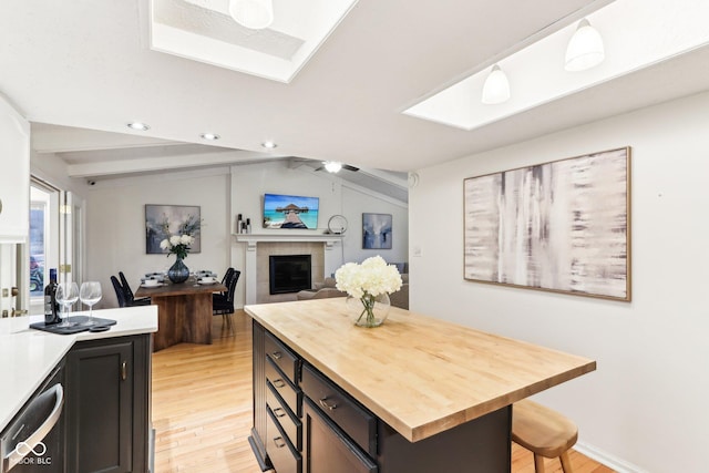 kitchen with light hardwood / wood-style flooring, a tile fireplace, wooden counters, dishwasher, and vaulted ceiling with skylight