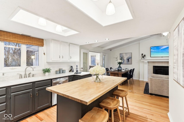 kitchen featuring a kitchen bar, sink, white cabinetry, dishwasher, and a fireplace